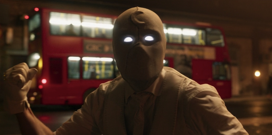Moon Knight, with glowing yellow eyes, stands in front of the number 25 bus