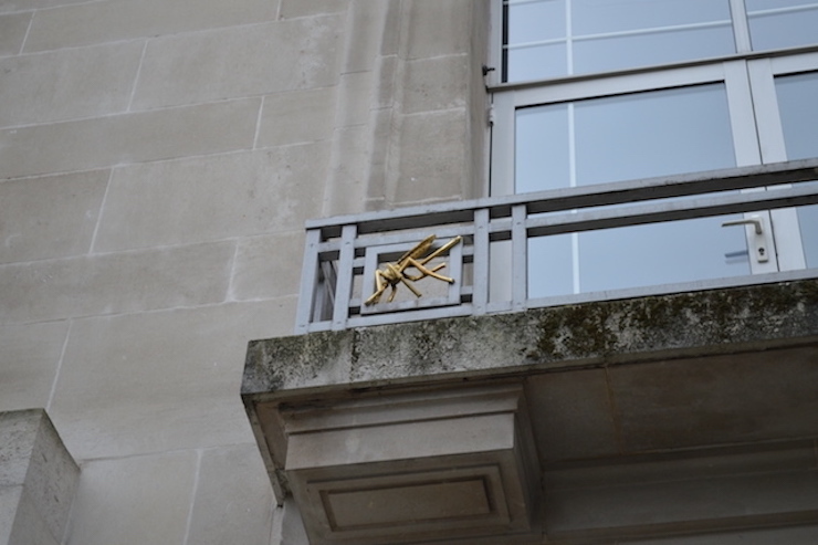 A balcony on a white stone building. It carries an ornamental golden mosquito

