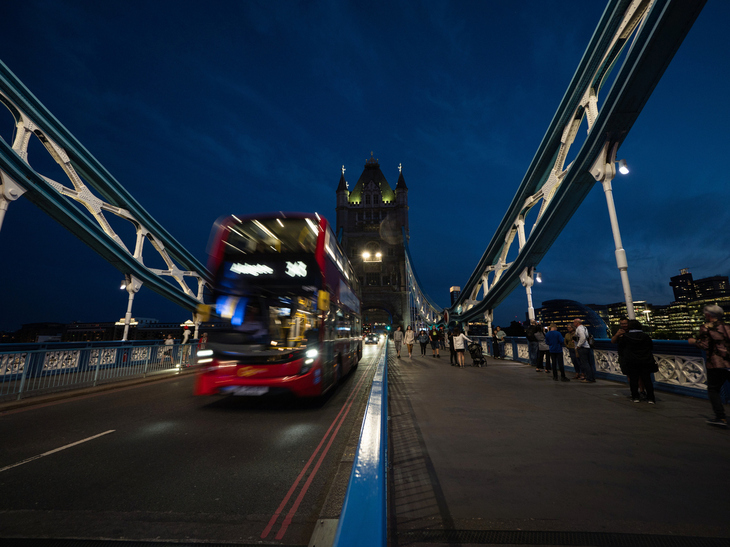 A red bus zooms over Tower Bridge, illuminated at night. 