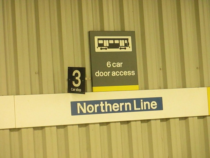 A 'Northern Line' sign on a corrugated metal wall, alongside another '6 car door access' sign