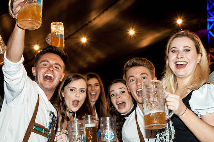 A group of young people raising beer steins to the camera
