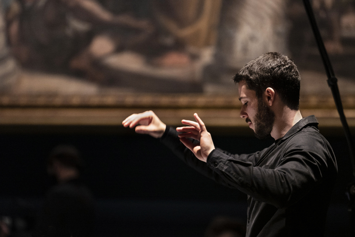 A conductor, facing to left, wielding his baton