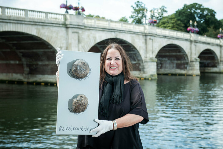 A woman holding up animal poo samples in front of Kingston Bridge