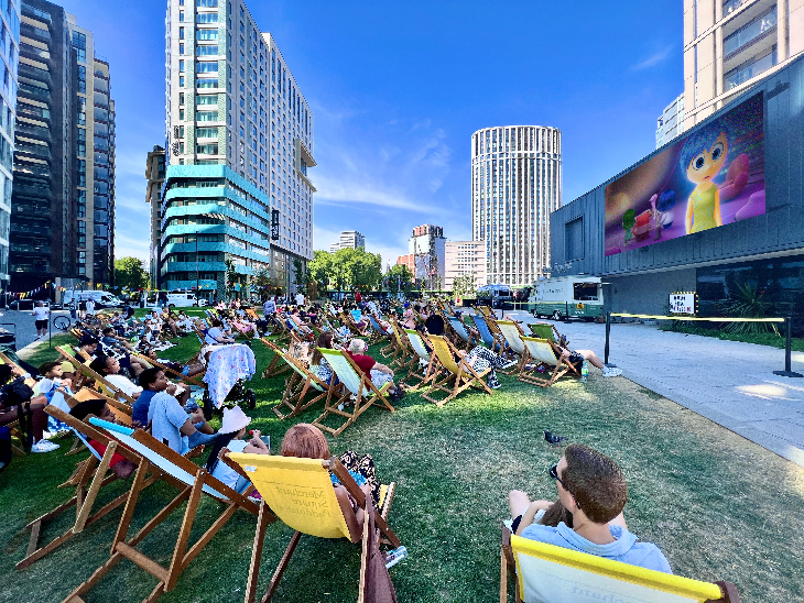 Open air cinema in London: people sitting on deckchairs watching a large screen at Merchant Square in Paddington.
