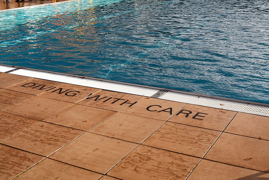 The edge of the pool at Parliament Hill Lido, with 'Diving with care' written on the terracotta-coloured floor tiles.