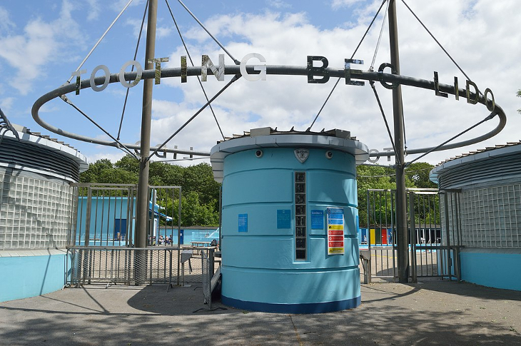 The entrance to Tooting Bec Lido - a blue coloured kiosk with a circular metal sign saying 'Tooting Bec Lido'