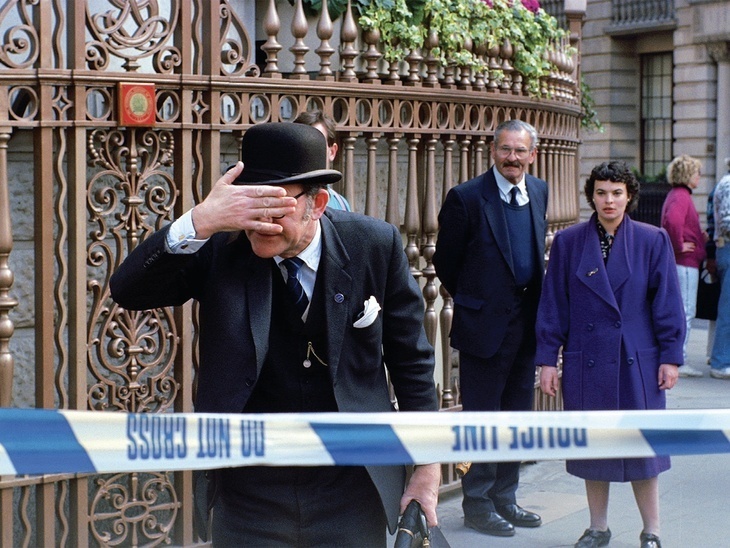 A bowler-hatted gent covers his eyes near some police tape