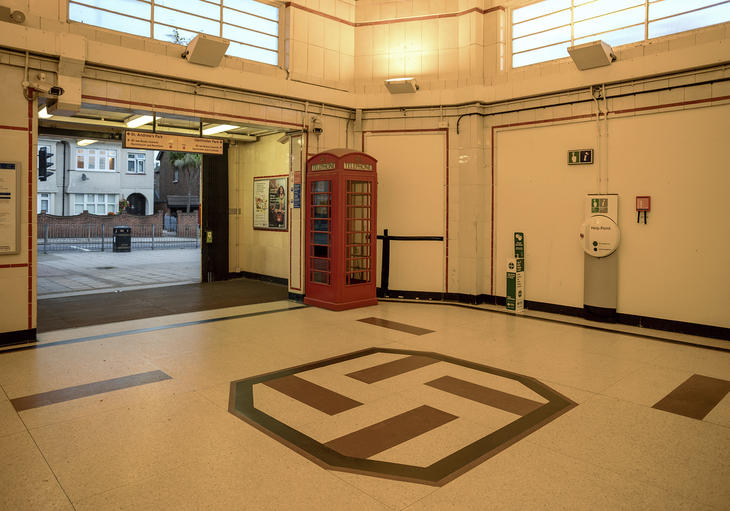 A tube ticket hall with a red phone box and a swastika on the floor