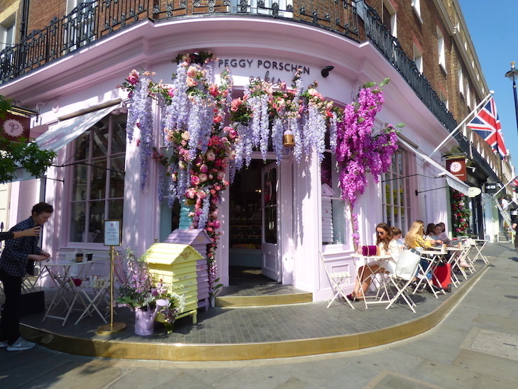 The exterior of Peggy Porshen Belgravia - a pale pink shopfront with purple and lilac fake flowers, including wisteria, hanging off of it.