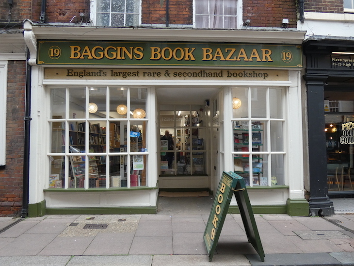 Book shop exterior: green amd yellow sign reading "Baggins Book Bazaar" and windows with white wooden cross frames