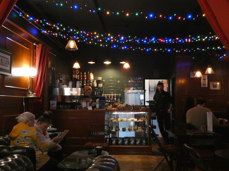 A dimly lit cafe with no natural light, a few small lamps, and strings of multicoloured fairy lights string across the ceiling