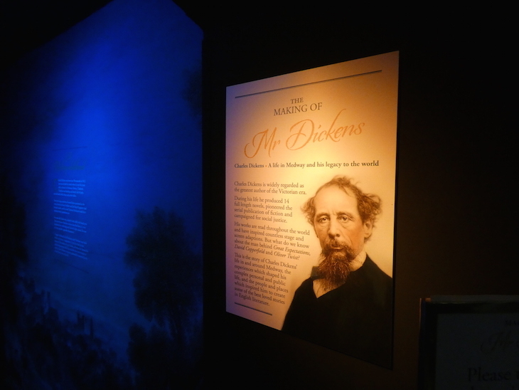 A dimly light room with an information panel about Charles Dickens illuminated by a spotlight