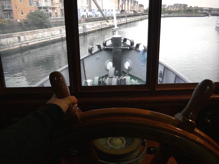 A hand steering a boat wheel, with a projection of the river shown in front, so it looks like you're driving the boat 