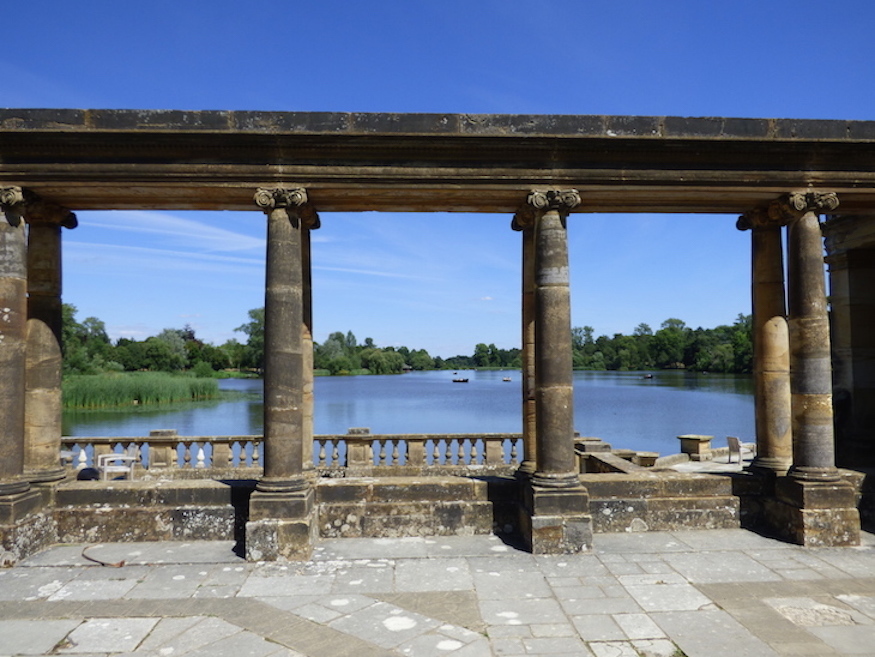 A view of a lake through a stone structure with ornate columns.