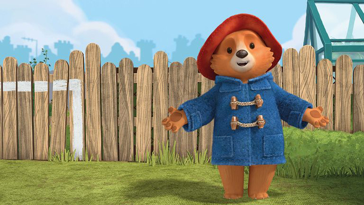 Paddington Bear standing in front of a brown fence on which a goal has been painted in white