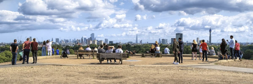 A photo of the summit of primrose hill with lots of people admiring the view
