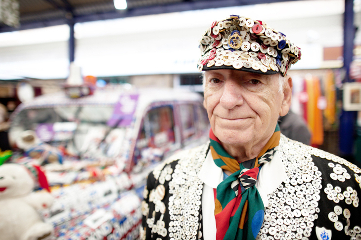 A pearly king in an outfit covered in sequins - with a pearly taxi cab in the background