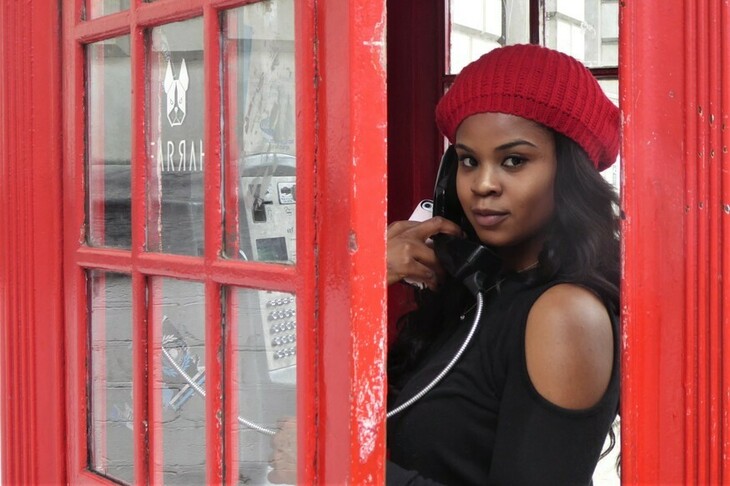 A woman in a red beret on the phone in a red phone box