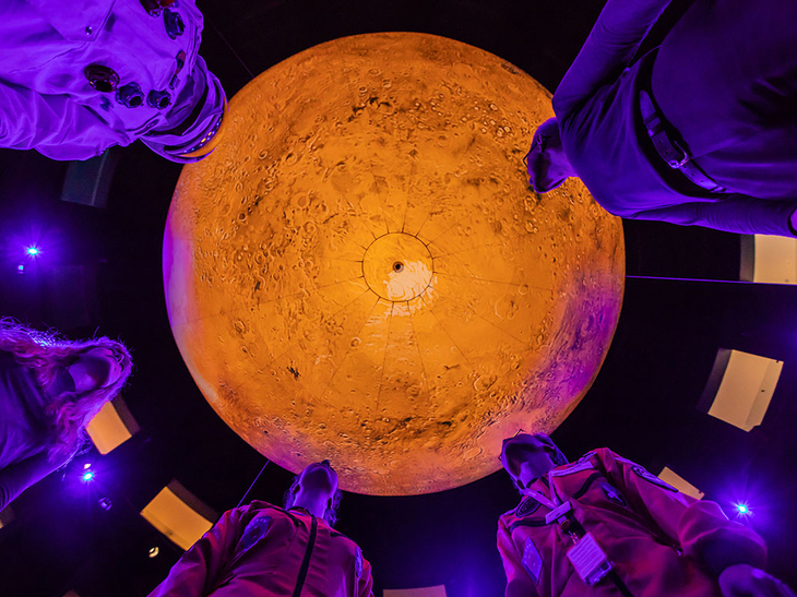Shot of four people stood beneath a glowing orange orb - as taken from below