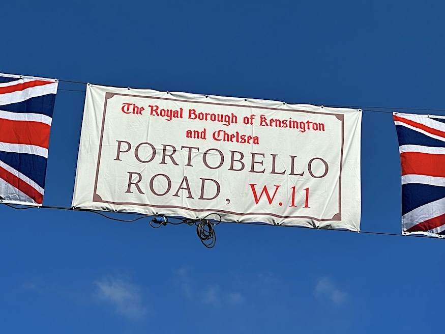 Portobello Road street sign printed onto a banner, hanging before a blue sky, with a union jack either side
