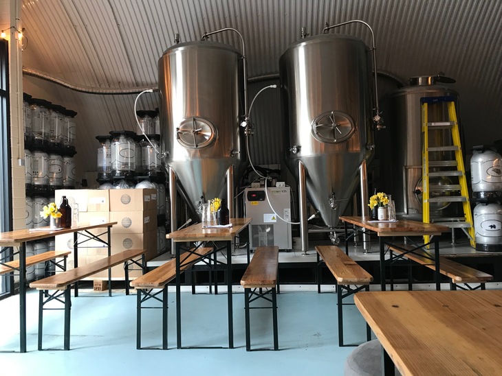 Brewery taprooms in London: A taproom with big silver fermenting tanks, and benches in front of them