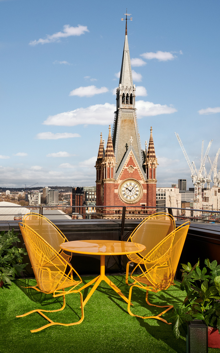 Best rooftop bars London: The neo gothic redbrick tower of St Pancras peeping over a terrace with yellow patio furniture