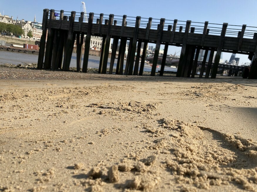 A sandy beach on the thames with a big jetty in the background