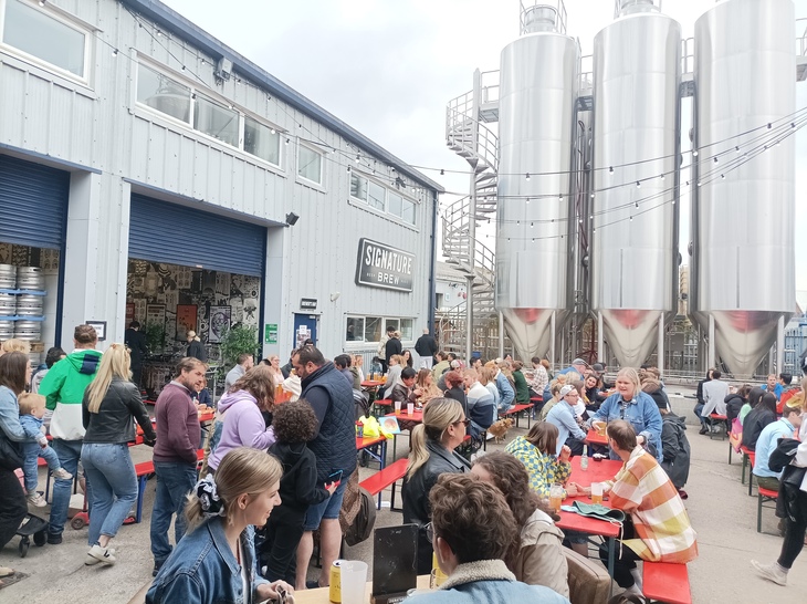 Brewery taprooms in London: People crowing outside a brewery with huge silver fermentation tanks in the background