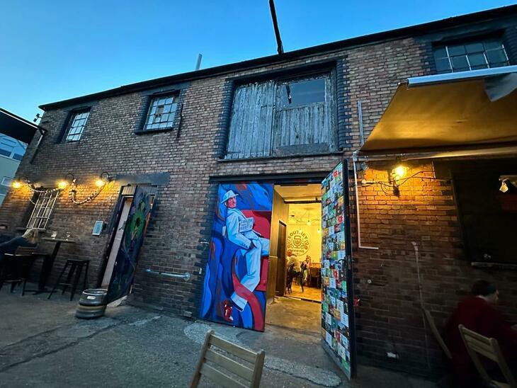 Brewery taprooms in London: A warehouse building with street art on the doors, and a bar illuminated inside
