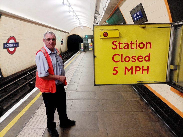 A bright yellow sign is pulled out by a man in high vis on the platform: 'station closed 5 mph'