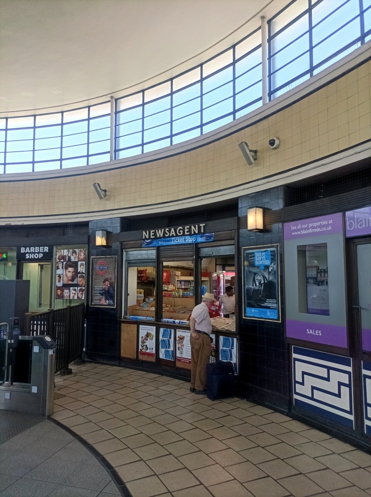 A gentleman purchases something from a newsagent inside the curved ticket hall space 
