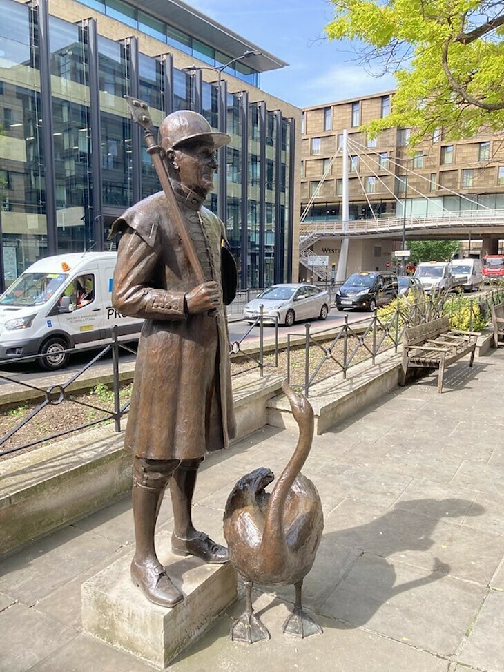 A swan marker in traditional uniform with a swan in sculptural form beside Thames Street