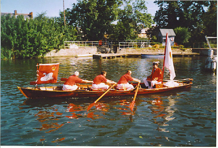 a party of swan uppers in red shirts rowing on the thames