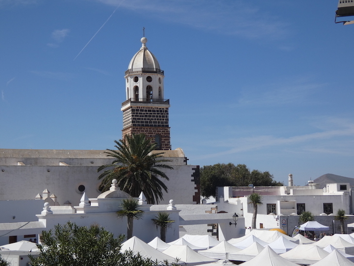 A brown church tower above a sea of white gazebos in a town square.