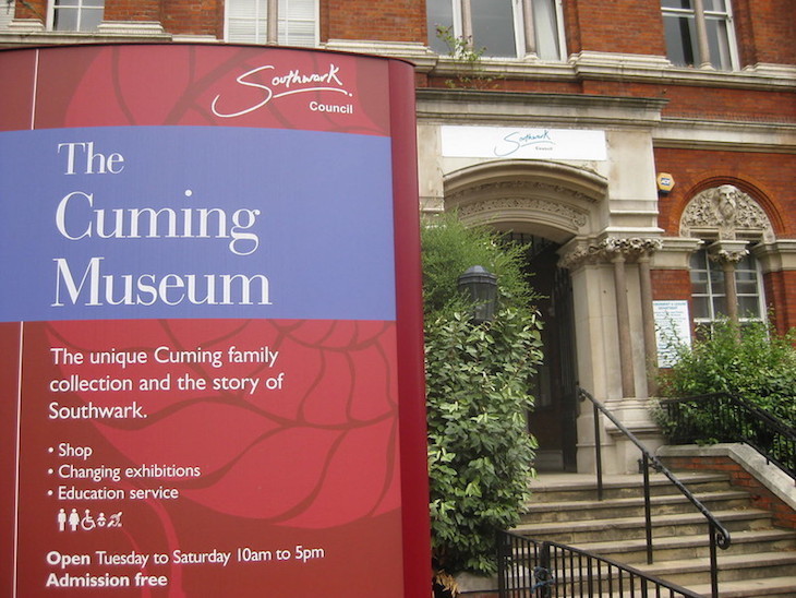 A red sign outside the former Cuming Museum building, with museum opening time information