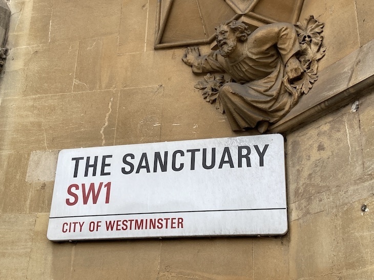 A street sign called The Sanctuary, with a reaching stone figure above
