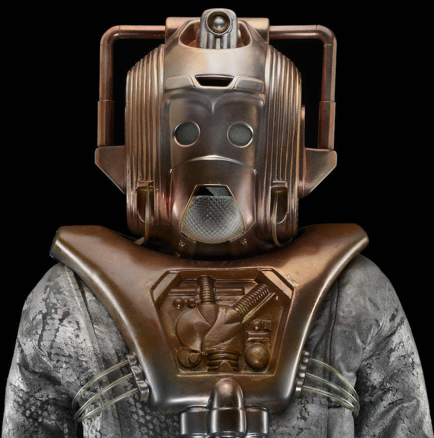 A bronze coloured Cyberman mask on a silver body suit