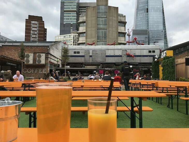 Vinegar Yard, Southwark, with lots of empty orange tables and some giant ants clambering on a train carriage