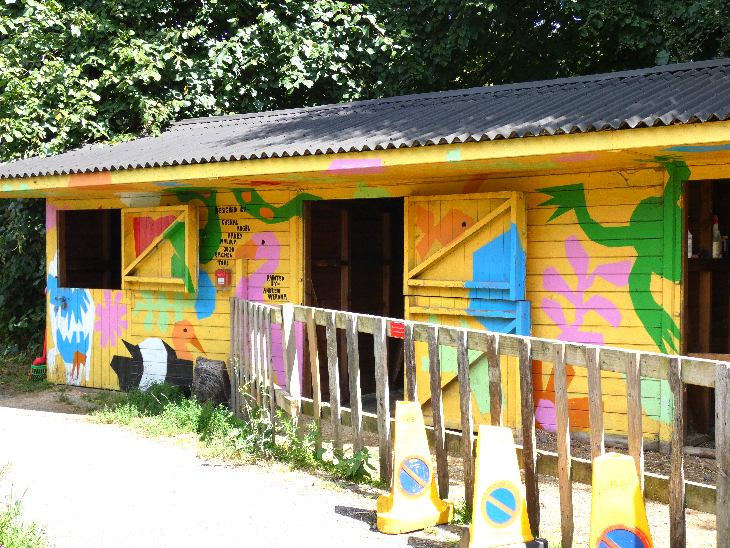 A stable painted a bright yellow with various animals and plants painted on in different colours.