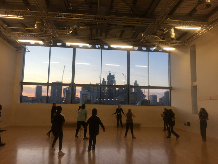 Girls training in a hall, with a City of London skyscape through the windows behind them