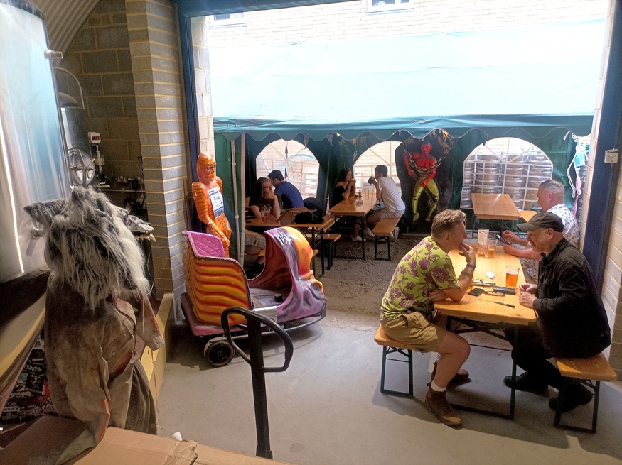 People drinking in a taproom, with a wolf mask and ghost car cab off to one side