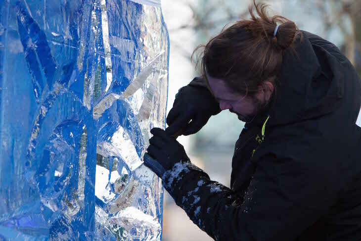 A man uses a chisel to sculpt a block of ice