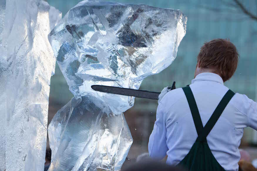 A man uses a chainsaw to carve a sculpture from a huge block of ice
