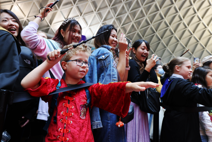 A young boy poses with a wand, with other Potter fans behind him in King's Cross station