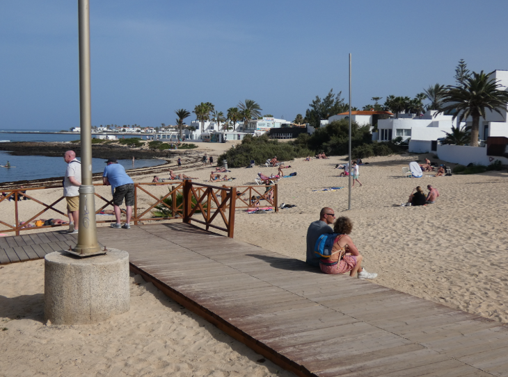 Corralejo in Fuerteventura: People sitting and standing on a wooden boardwalk on Corralejo town beach
