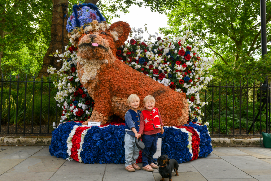 Chelsea in Bloom: two young boys and a dog pose in front of a giant corgi made from flowers