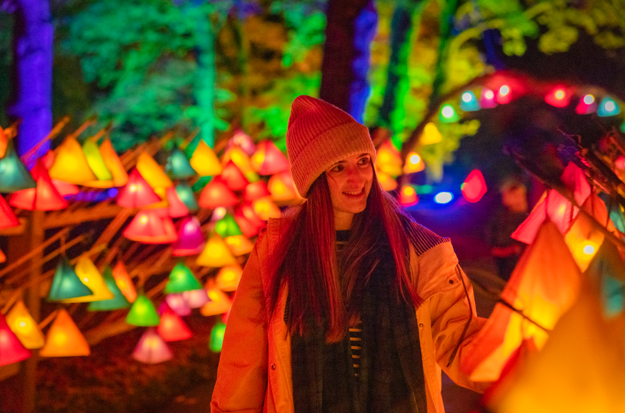 A woman in a woolly hat walking past a wall of lanterns in various colours.