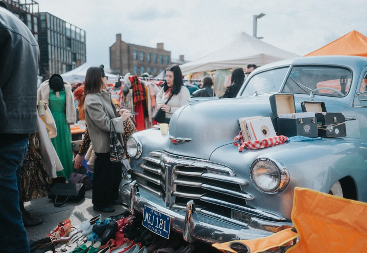 A classic car parked up among stalls selling vintage clothes