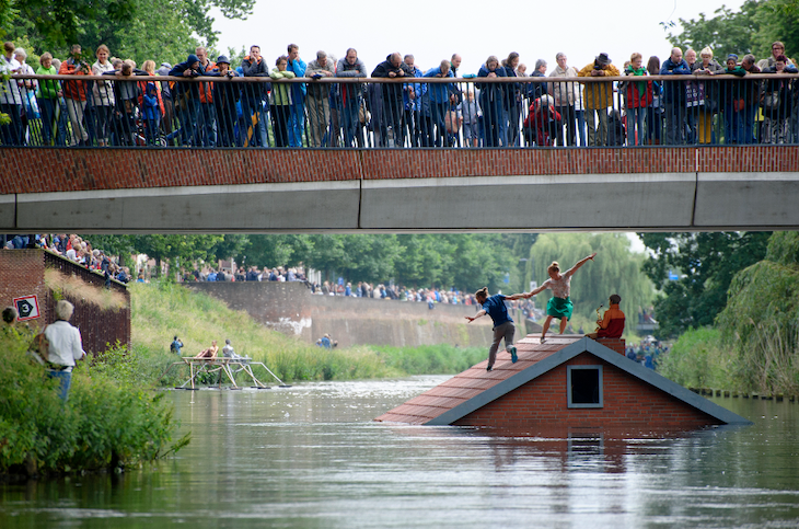 A house submerged in water with a bridge over the top full of people