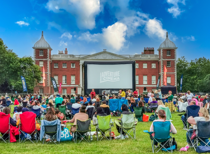 Open air cinema in London: An Adventure Cinema screen erected on the lawn in front of Osterley House, with people sitting on camping chairs watching
